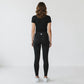 Woman wearing Mercifully Made black high-waist leggings with black tee, rear view