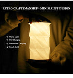 White collapsible lantern lamp with geometric origami-style fold pattern illuminated in warm light