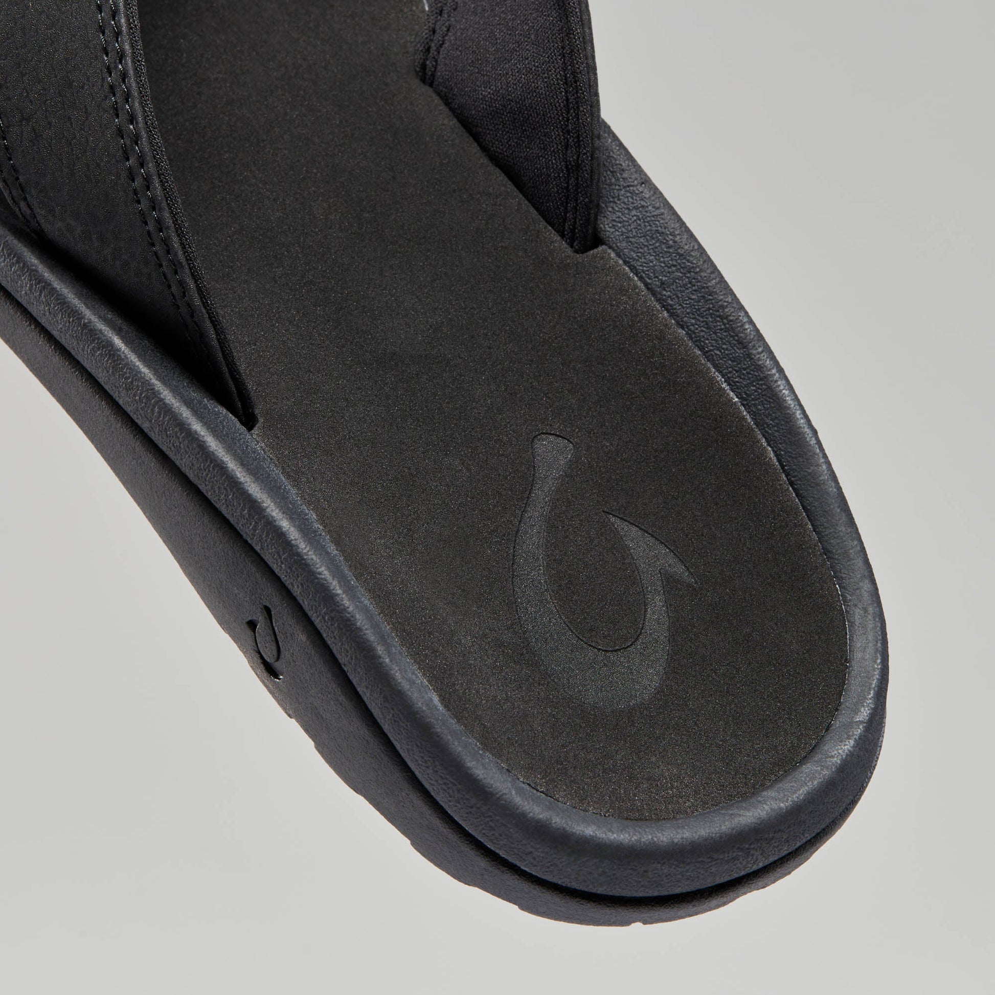 OluKai Men's Ohana black sandal close-up showing footbed and fish hook logo detail