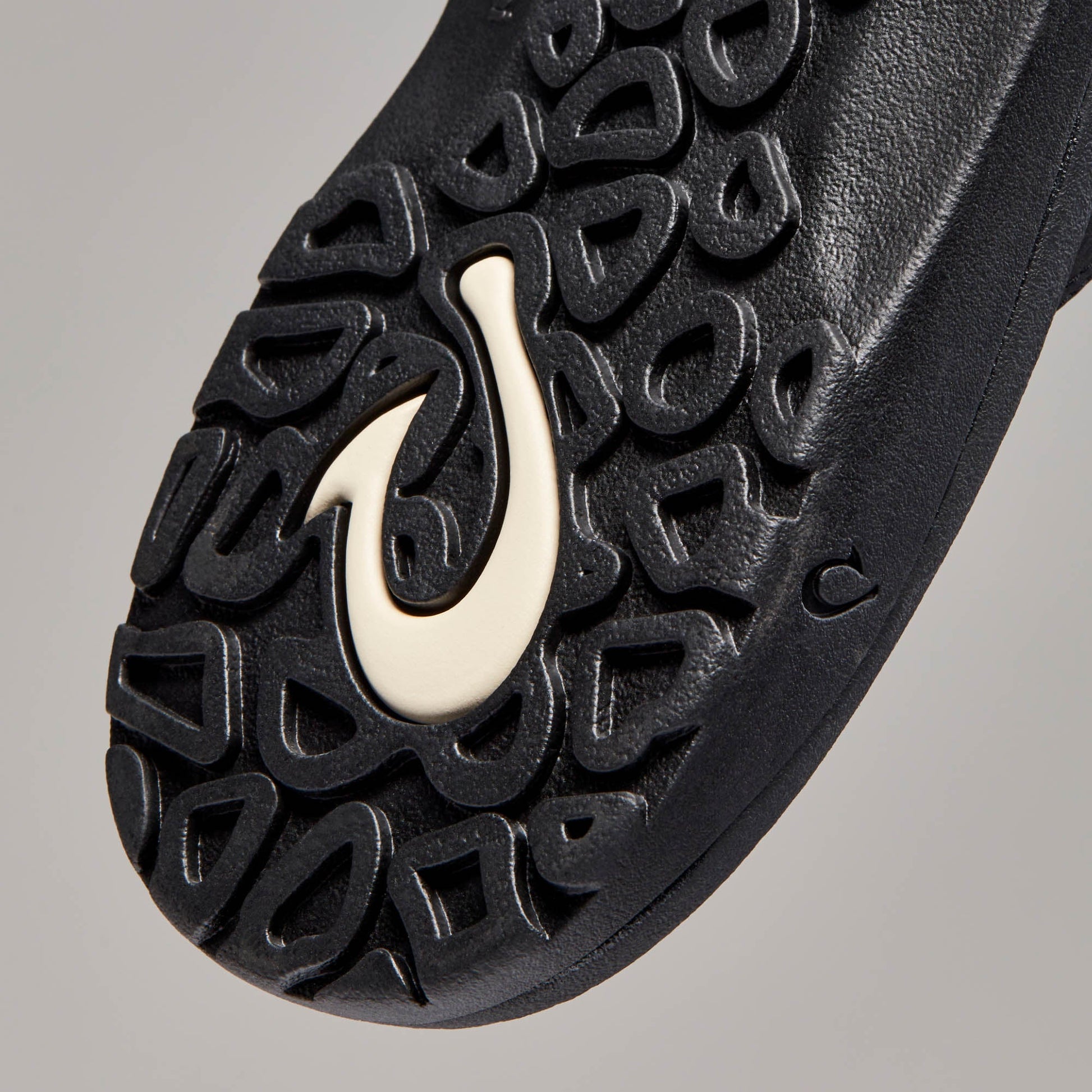 Close-up of OluKai Ohana black sandal outsole with textured tread pattern and cream logo