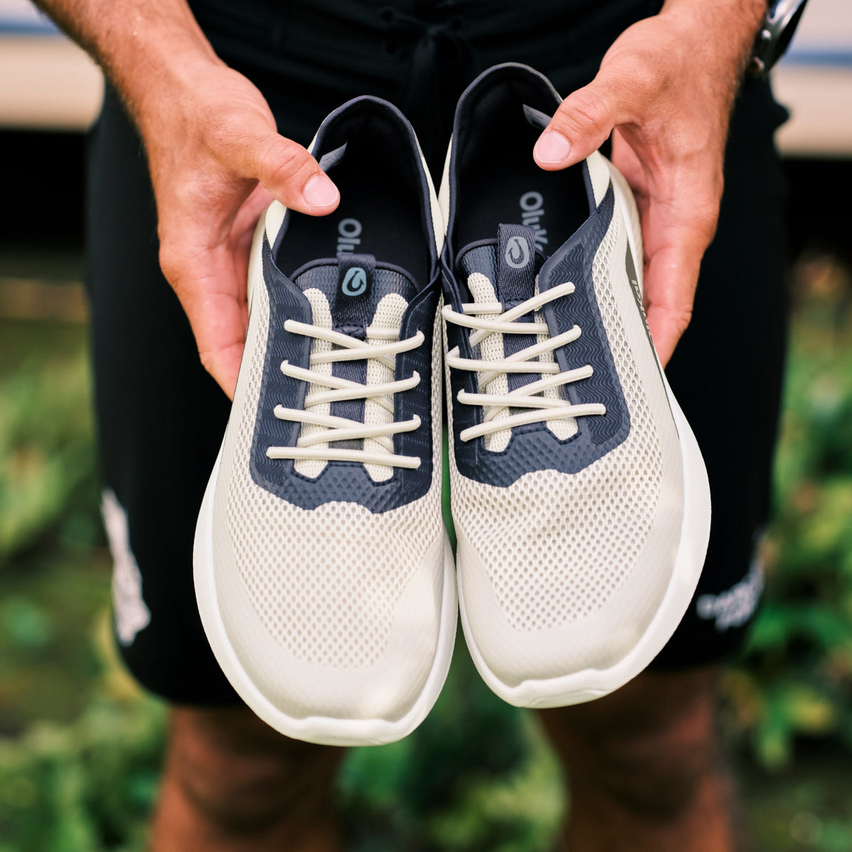 OluKai Men's Kialoa sneaker in Tapa cream mesh with Trench Blue overlay held by hands