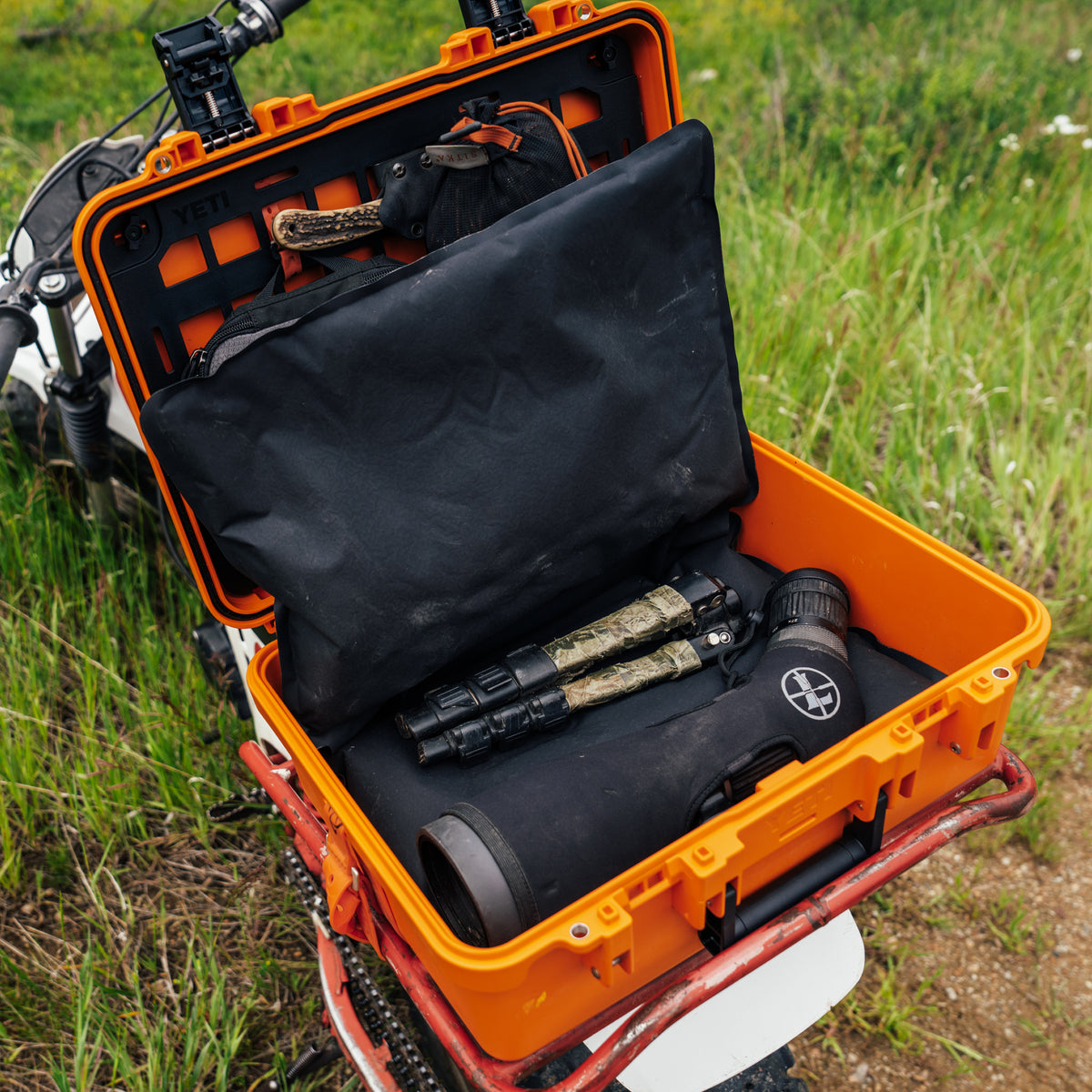 YETI Loadout GoBox orange protective case open on motorcycle showing black interior inserts and optics gear