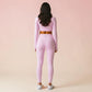 Woman wearing light rose pink long-sleeve crop top and matching high-waist leggings, rear view