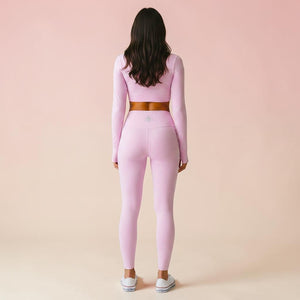 Woman wearing light rose pink long-sleeve crop top and matching high-waist leggings, rear view