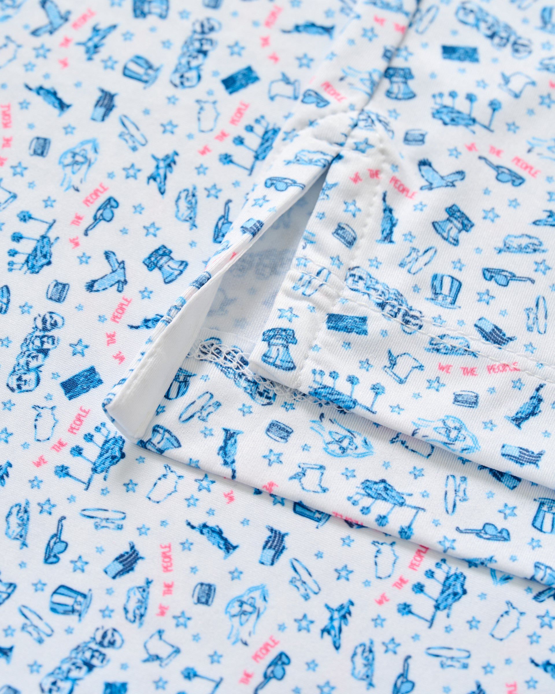 White polo shirt with blue and pink printed pattern of various icons and stars