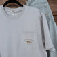 Coastal Cotton Mallard Tradewind Tee in light blue-gray with chest pocket logo, styled with jeans