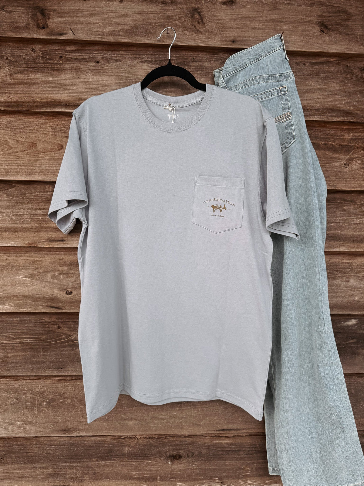 Coastal Cotton Mallard Tradewind pocket tee in light gray-blue hanging on wooden wall