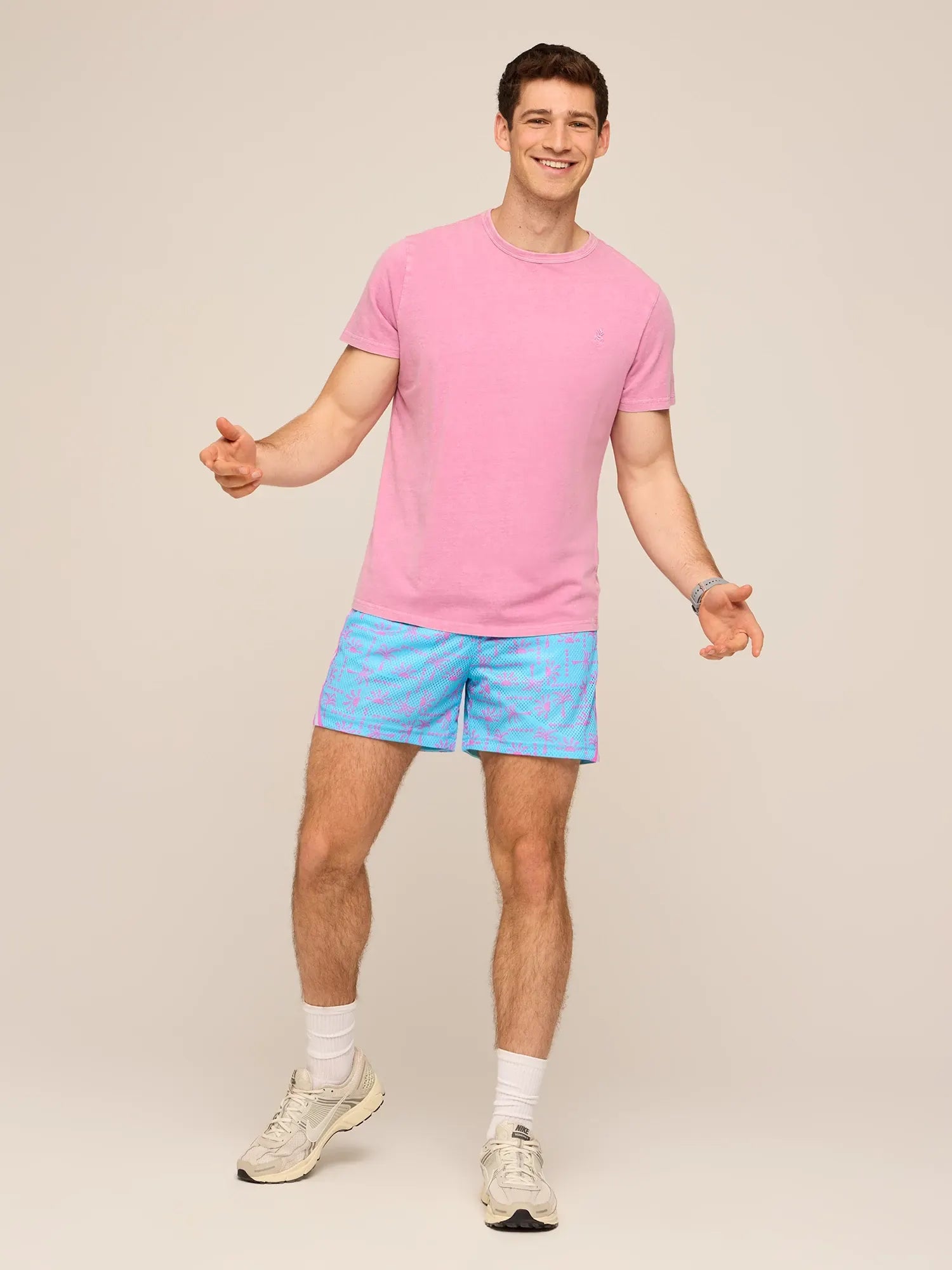 Man wearing pink t-shirt and dusty blue patterned swim trunks with white sneakers