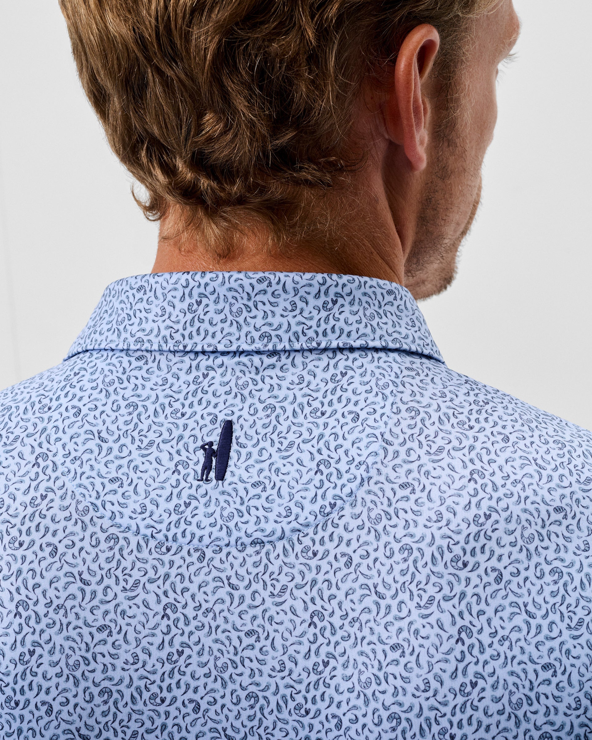 Back view of man wearing light blue polo shirt with navy paisley pattern