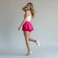 Woman wearing white tank top and bright pink Grace in Motion athletic skort with white sneakers