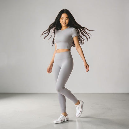 Woman wearing gray crop top and matching high-waist leggings with white Converse sneakers