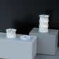 Illumates Large Lamp in white with geometric twisted design displayed on white pedestals